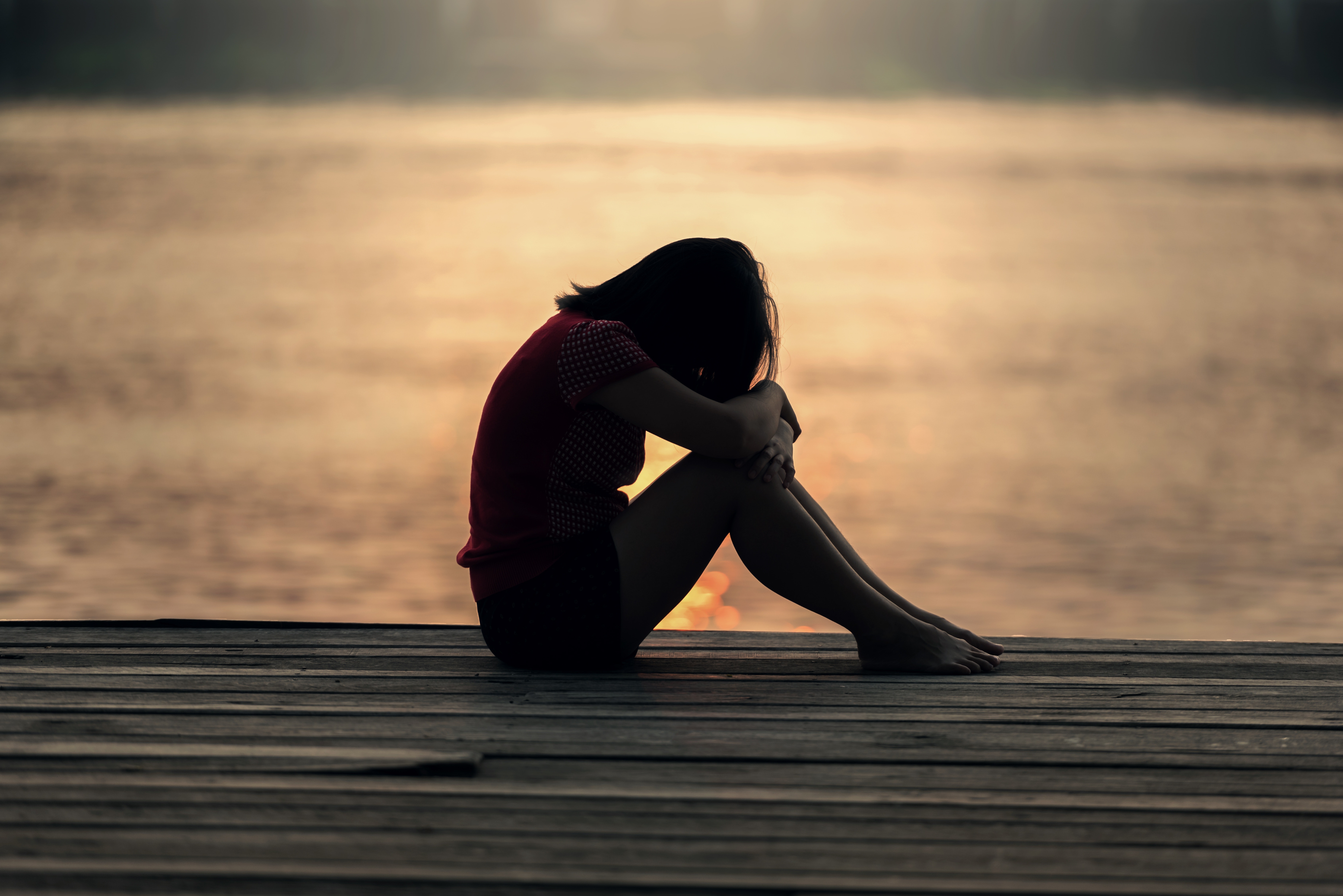 A girl sits on a dock with her head on knees feeling distressed. She has decided to pursue trauma therapy in Forest Hills, NY with trauma therapist Deborah Karnbad. You can also get online counseling with trauma therapy in New York too!