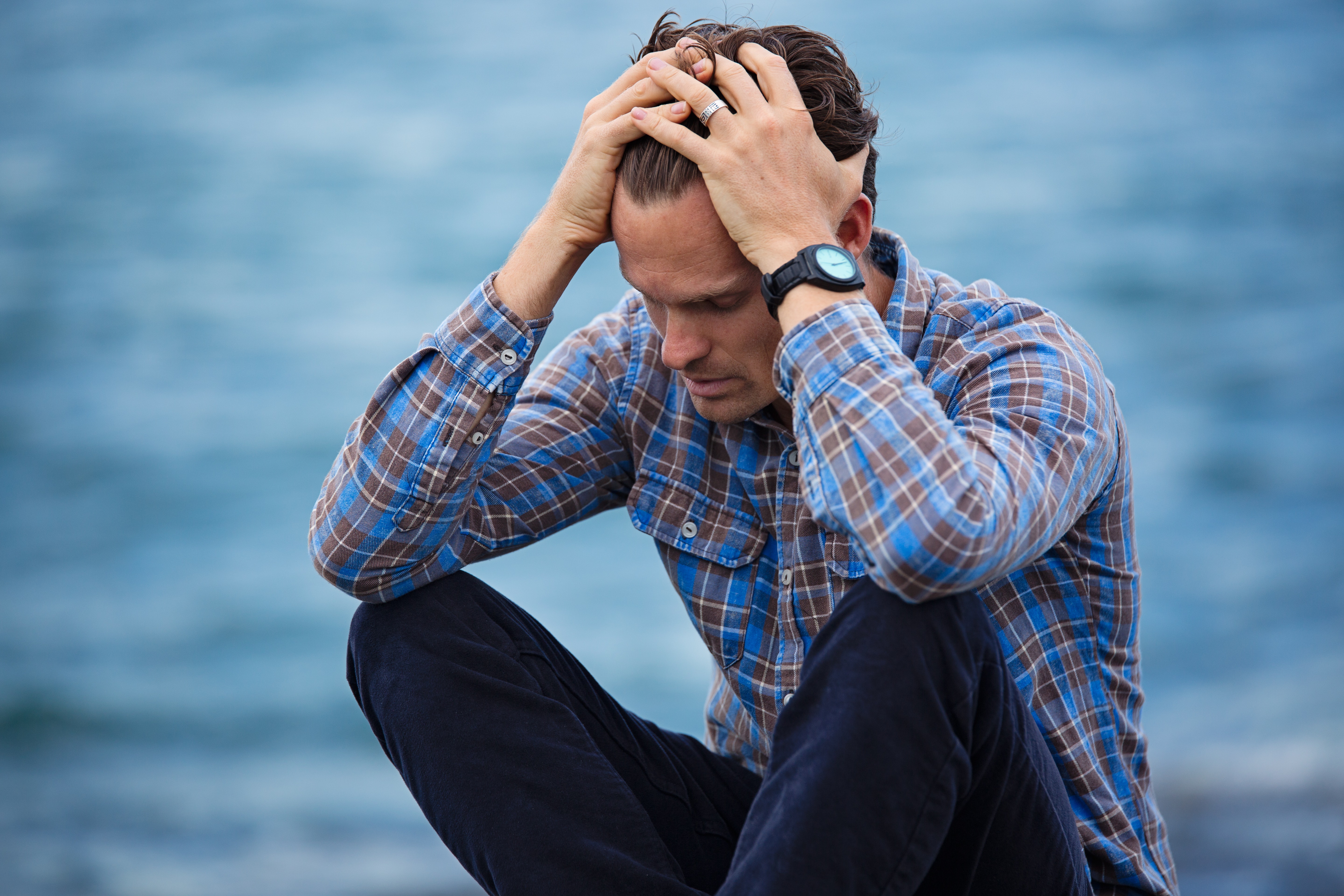 A man sits with his head in his hands, feeling overwhelmed. He has decided to start counseling for stress in New York with Deborah Karnbad.