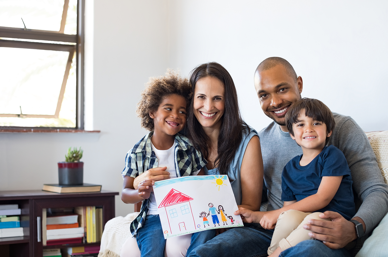 A family of four sits together smiling. They feel more connected after beginning counseling for step parents in Forest Hills, New York with therapist Deborah Karnbad.