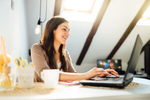 A woman smiles while using her laptop. She has started online therapy in New York for trauma therapy, couples counseling and counseling for divorce step parents with Deborah Karnbad. 