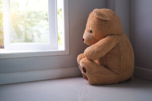 A stuffed bear sits next to the window, looking sad. This is an example of sadness is a common reason why people pursue online therapy in New York with Deborah Karnbad who specializes in trauma therapy in forest hills, ny and beyond.. 