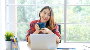 A woman smiles while using her laptop. She is happy with her decision to pursue online therapy for college students in New York with Deborah Karnbad who specializes in trauma therapy in forest hills, ny. 