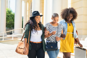 Three female college students walk while holding arms. They are happy with their decision to pursue online therapy for college students in New York with Deborah Karnbad.