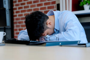 A man has his head on his desk feeling sad. He is looking forward to starting depression counseling in Long Island, NY with Deborah Karnbad.