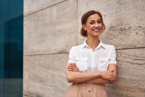 A woman smiles while leaning against a wall. She is feeling much happier since starting depression counseling in Long Island, NY with Deborah Karnbad. 