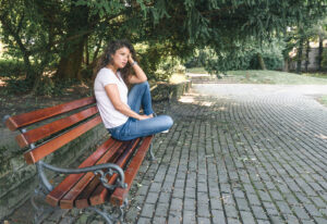 A girl sits on a bench looking upset. She is looking forward to starting online marriage counseling in New York with Deborah Karnbad.