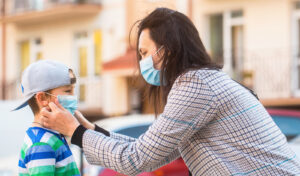 A mother puts a mask on her son. This is similar to parent counseling in Forest Hills, NY.